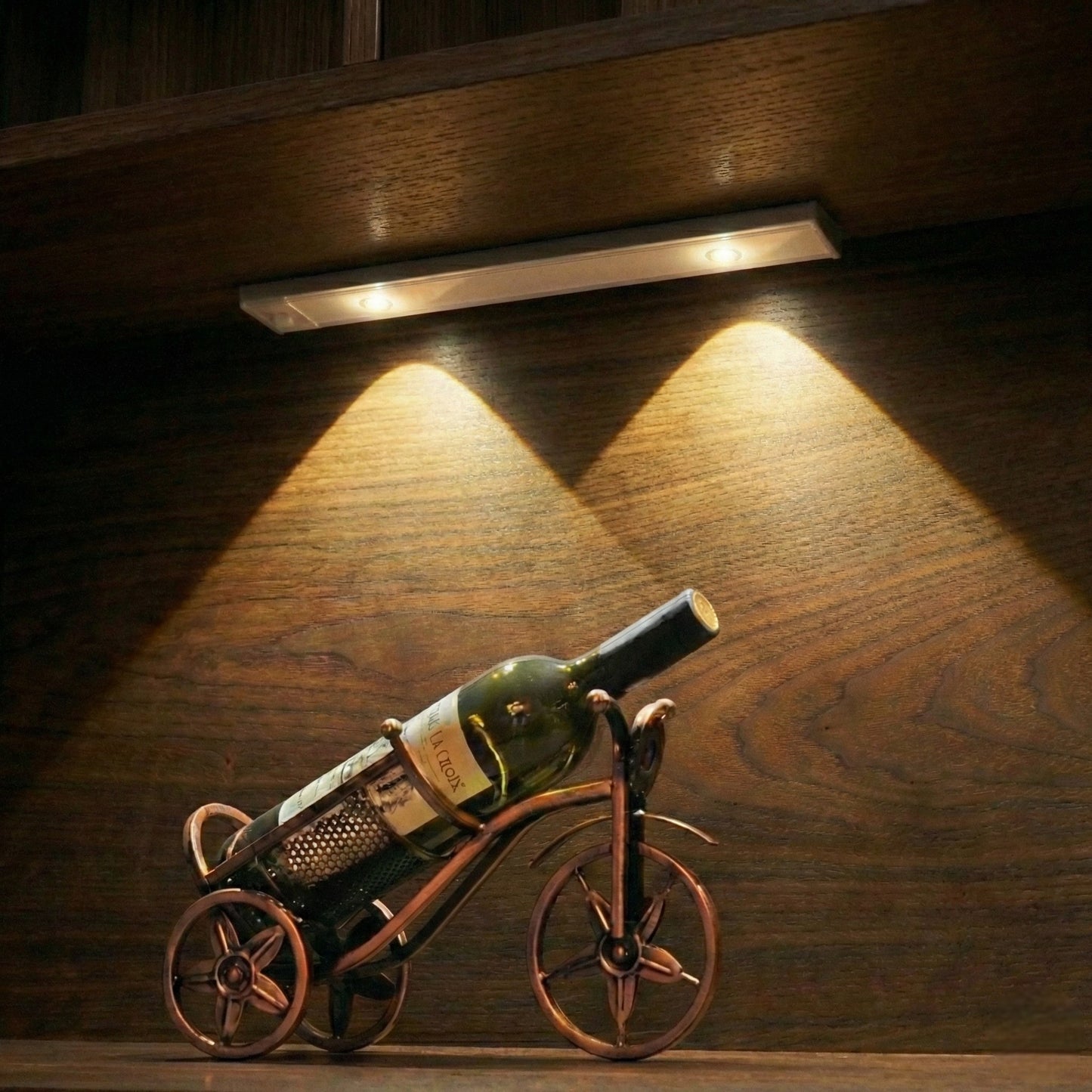 Wine bottle on a decorative metal bike stand under a wooden cabinet light.