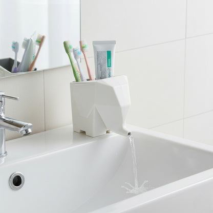 White elephant-shaped toothbrush holder on a bathroom sink with toothbrushes and toothpaste.