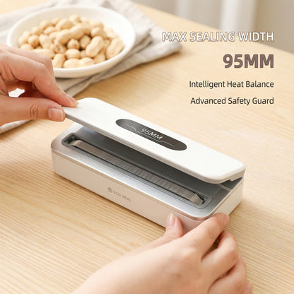 Hand using a food vacuum sealer on a wooden table with a bowl of peanuts in the background.