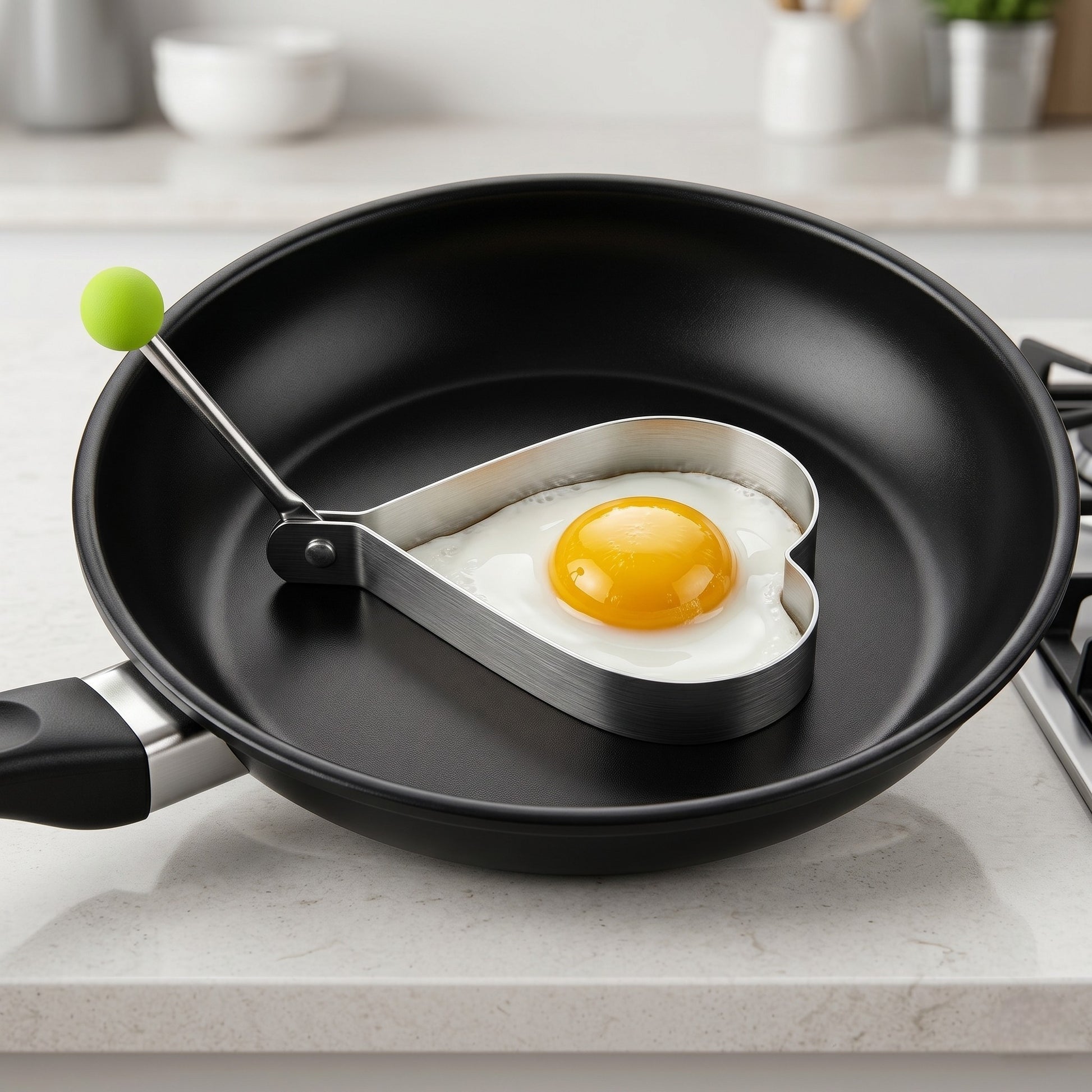Heart-shaped egg tool in a frying pan with a fried egg on a kitchen counter.