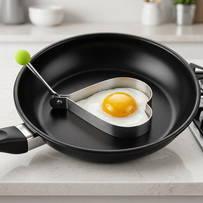 Heart-shaped egg tool in a frying pan with a fried egg on a kitchen counter.