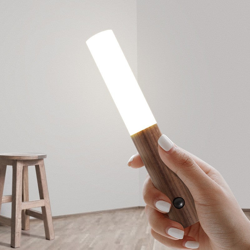 Hand holding a wooden flashlight with a white light on a neutral background