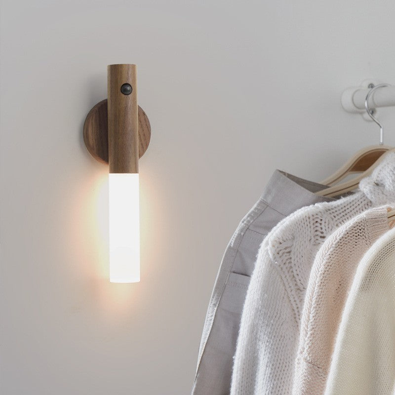 Wooden wall sconce with a light fixture next to hanging clothes on a rack.