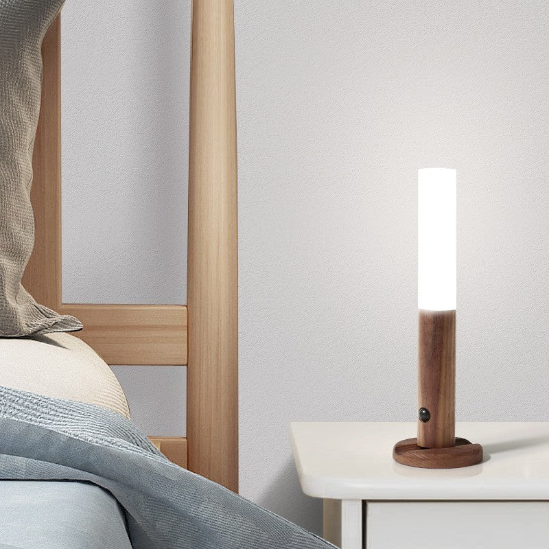 Wooden lamp on a nightstand next to a bed with light bedding.
