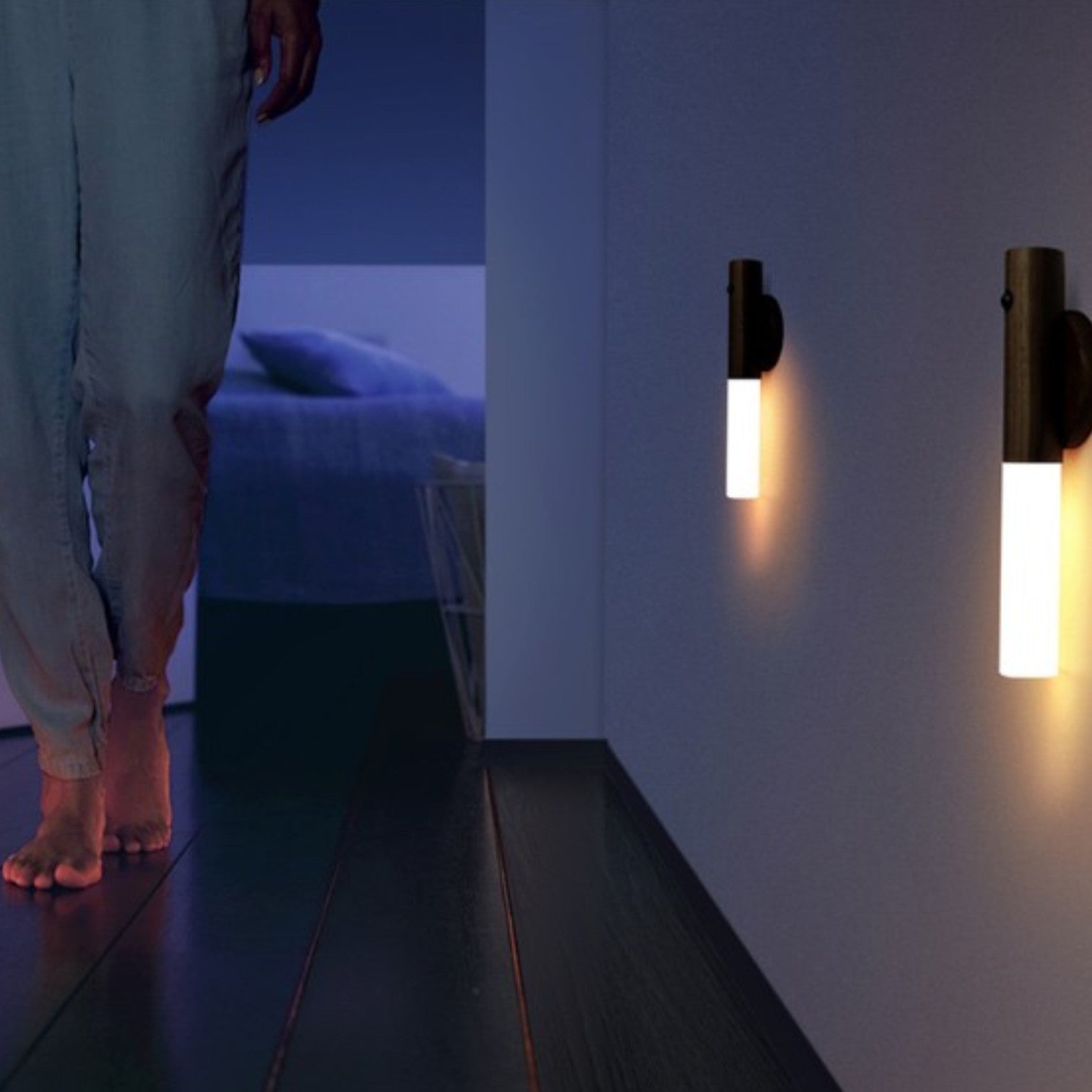 Person standing in a bedroom with two wall-mounted lights on a dark wall.