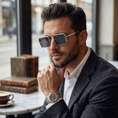Man wearing sunglasses and a watch, sitting at a table with a cup of coffee.