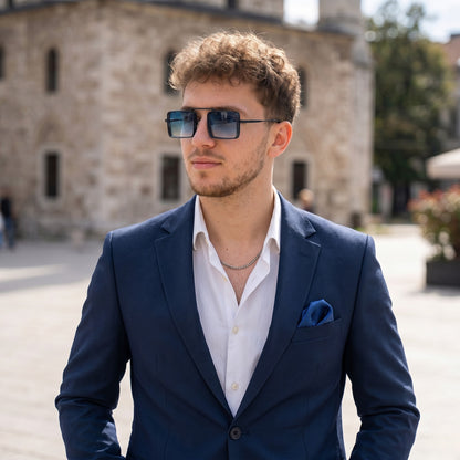 Man wearing a blue suit and sunglasses outdoors with a building in the background