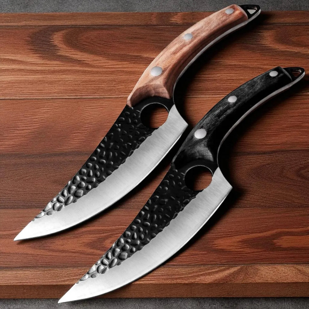 Two curved kitchen knives with hammered steel blades and different handle finishes, displayed diagonally on a dark wood background.