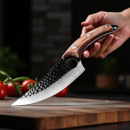 Hand holding a knife with a wooden handle on a wooden cutting board with tomatoes in the background