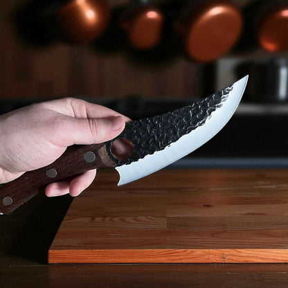 Hand holding a knife with a wooden handle on a wooden surface