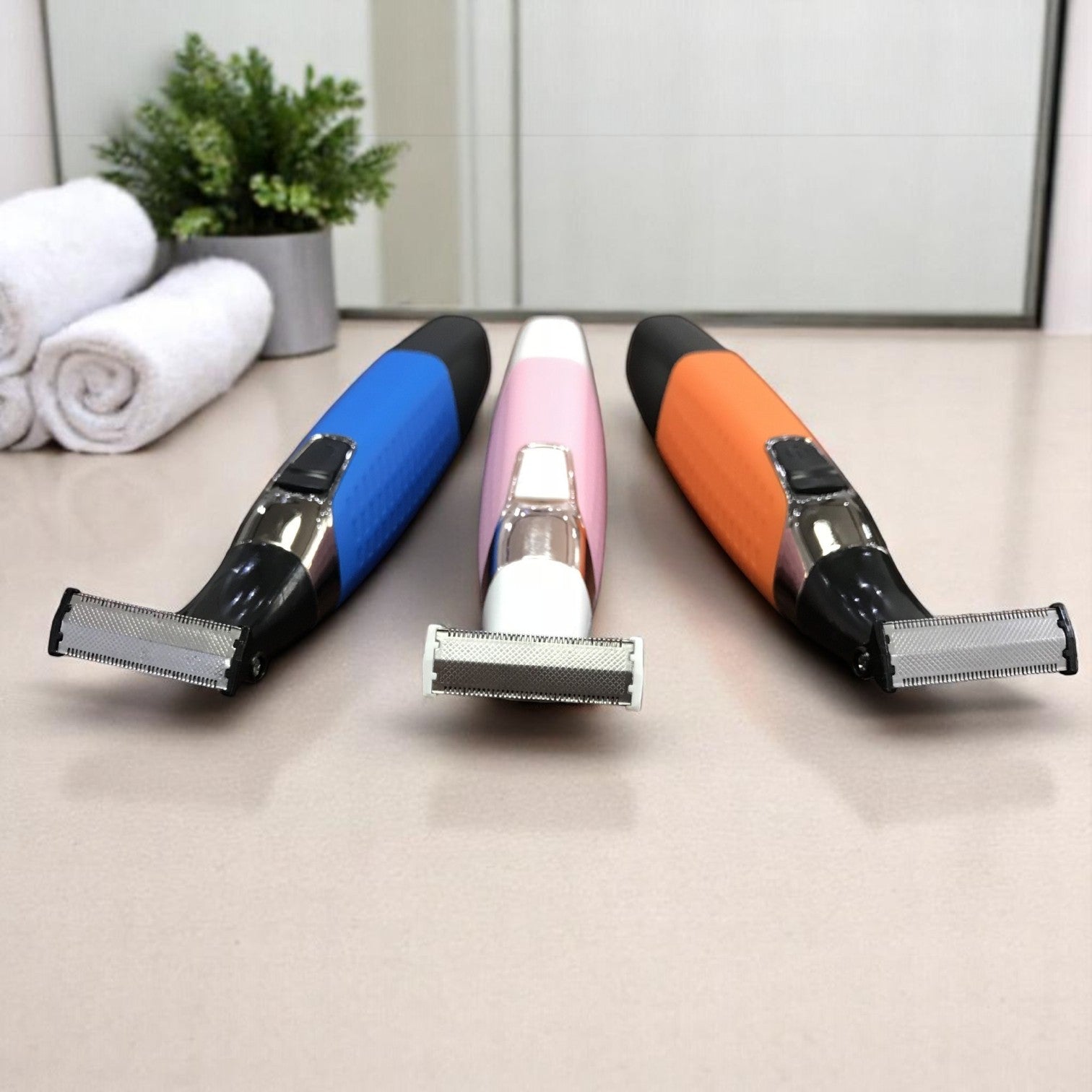 Three colorful razors on a counter with a mirror and towels in the background.