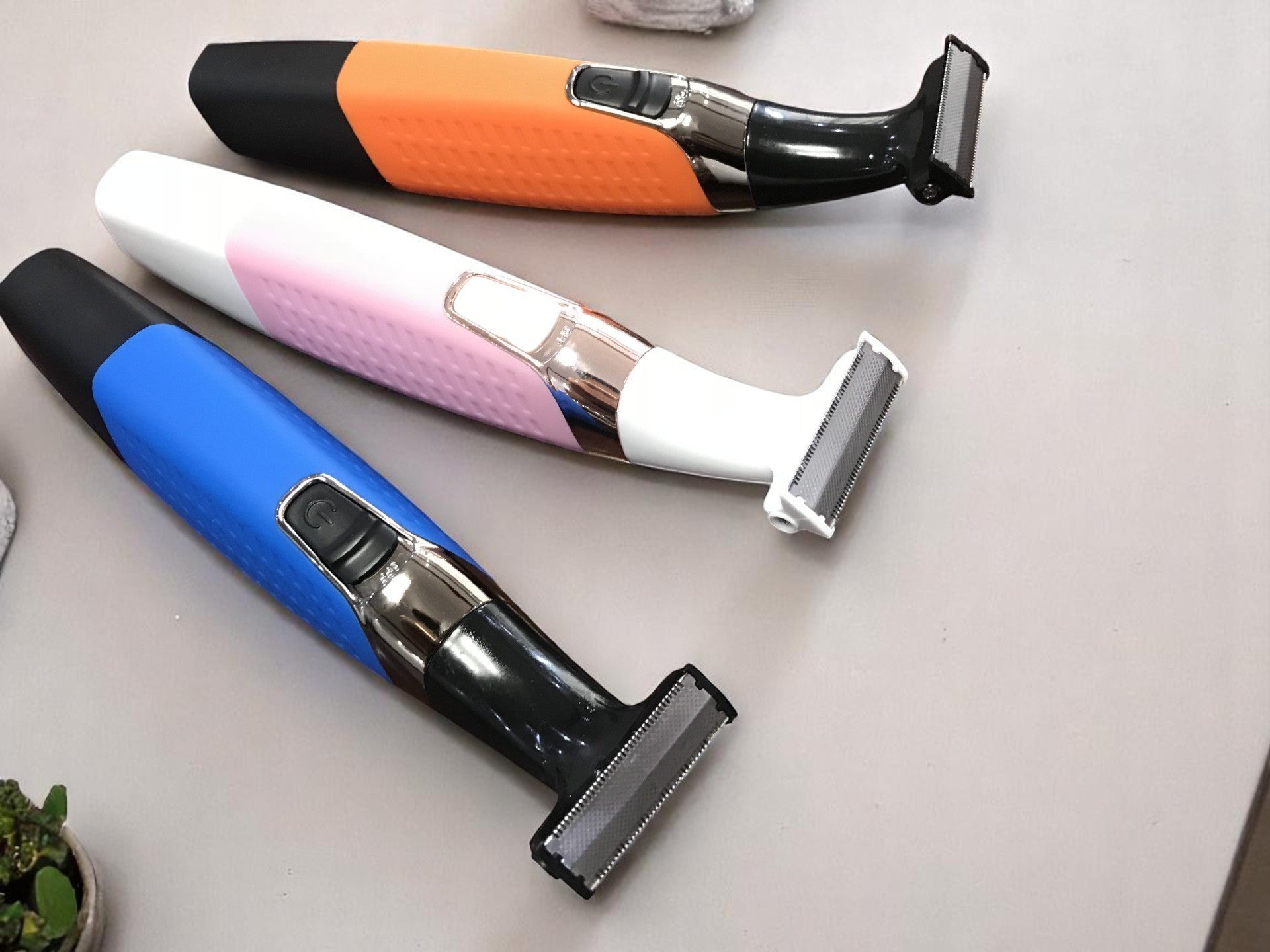 Three electric razors in blue, pink, and orange on a white surface.